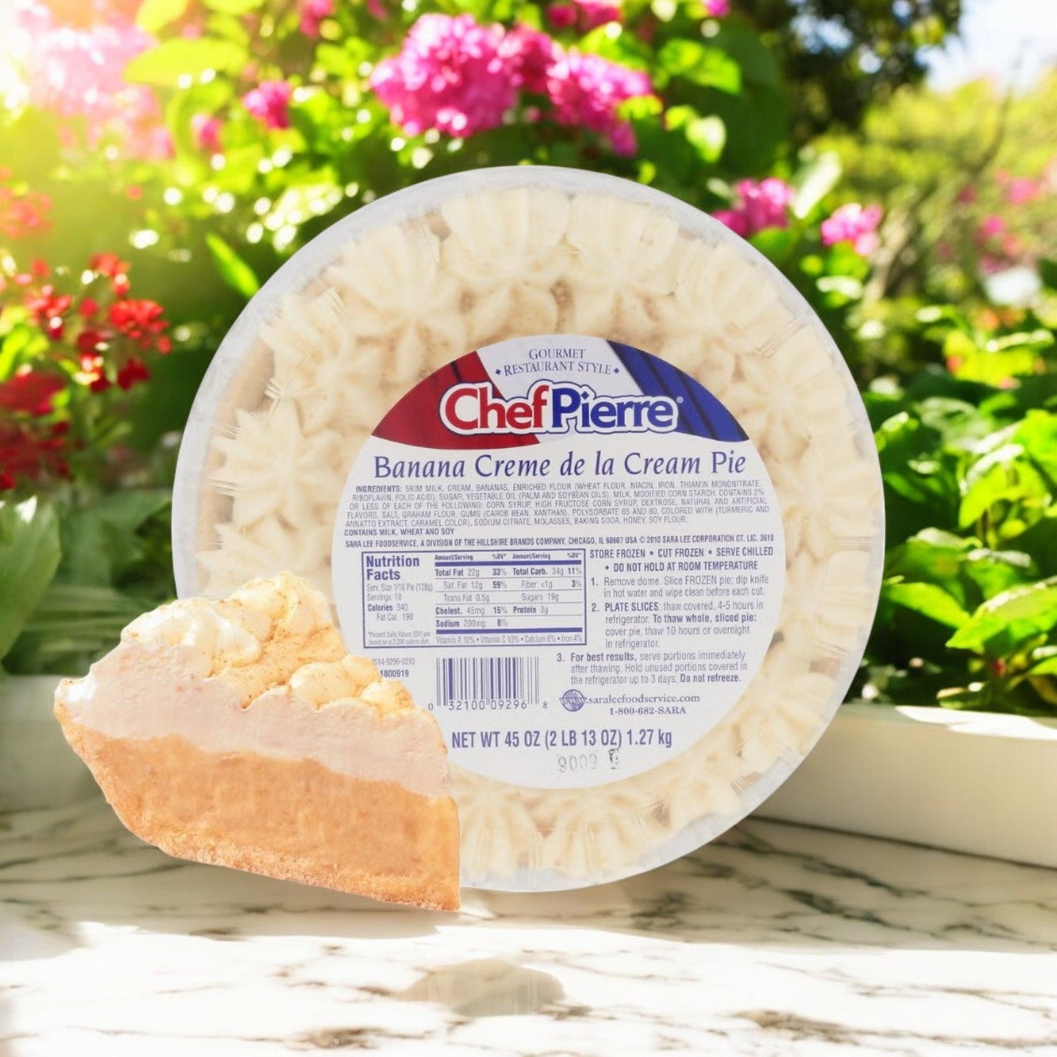 A whole Chef Pierre Banana Creme de la Cream Pie with a slice cut out, displayed on a marble surface with a garden background.