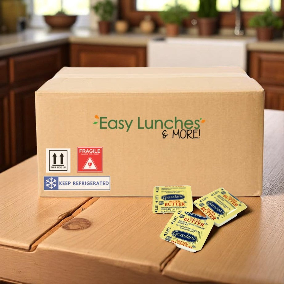 A cardboard box labeled "Grassland Salted Butter Portion Cups – 720 Count" sits on a kitchen counter with four individually packaged Grassland Grade AA salted butter cups arranged in front for convenience.