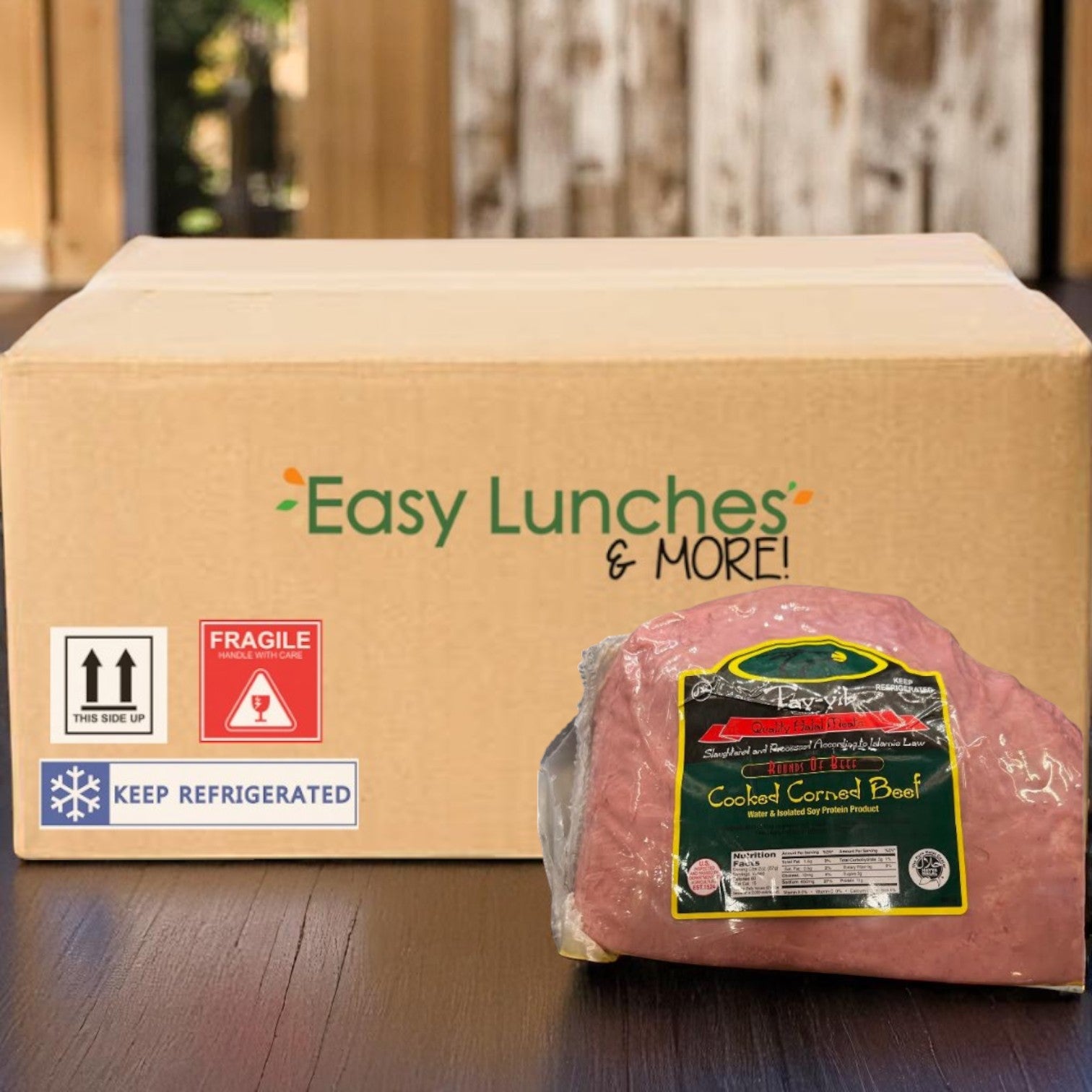 A cardboard box labeled "Easy Lunches" sits behind a vacuum-sealed package of Tay-Yib Halal Corned Beef (7 lbs average, 1 case) on a wooden surface.