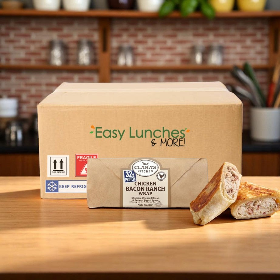 A "Clara's Kitchen Individually Wrapped Chicken, Bacon & Ranch Wrap - 8 oz. (12 Pack Case)" box rests on the kitchen counter, featuring a delectable wrap and two tempting wrap halves, amidst cooking utensils and a brick backsplash.