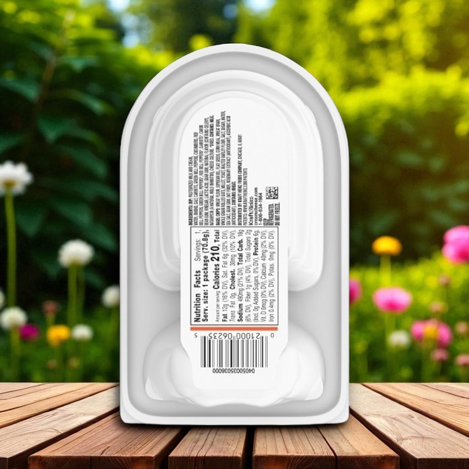 The Kraft Philadelphia Multigrain Bagel Chips & Garden Vegetable Cream Cheese Dip (2.5 oz.) snack pack rests on a wooden surface, its label showing nutrition facts and a barcode, with a blurred garden in the background.