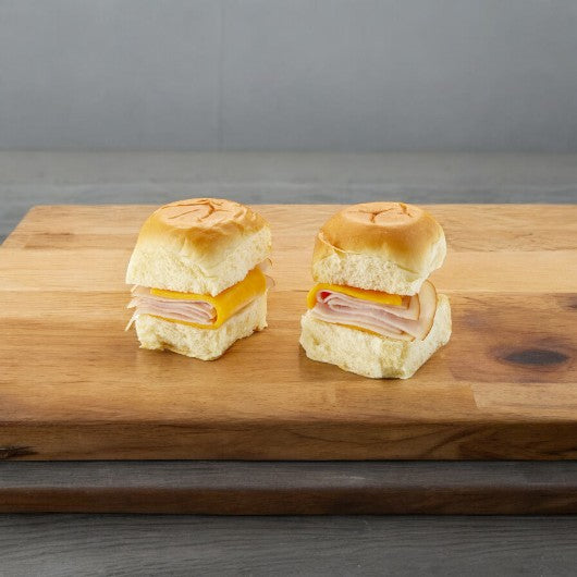 Two E.A. Sween Smoked White Turkey and Cheddar Sliders are neatly presented on a wooden board, shipped frozen with a 30-day cooler shelf life.