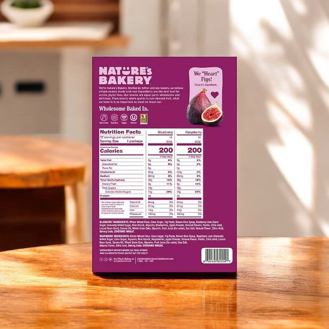 The Nature's Bakery Fig Bars, Variety Pack-32 Count-1 Pack box, features nutritional facts and ingredients. The purple box with fig images emphasizes these bars are made with Whole Grains and Real Fruit, displayed on a rustic wooden table.