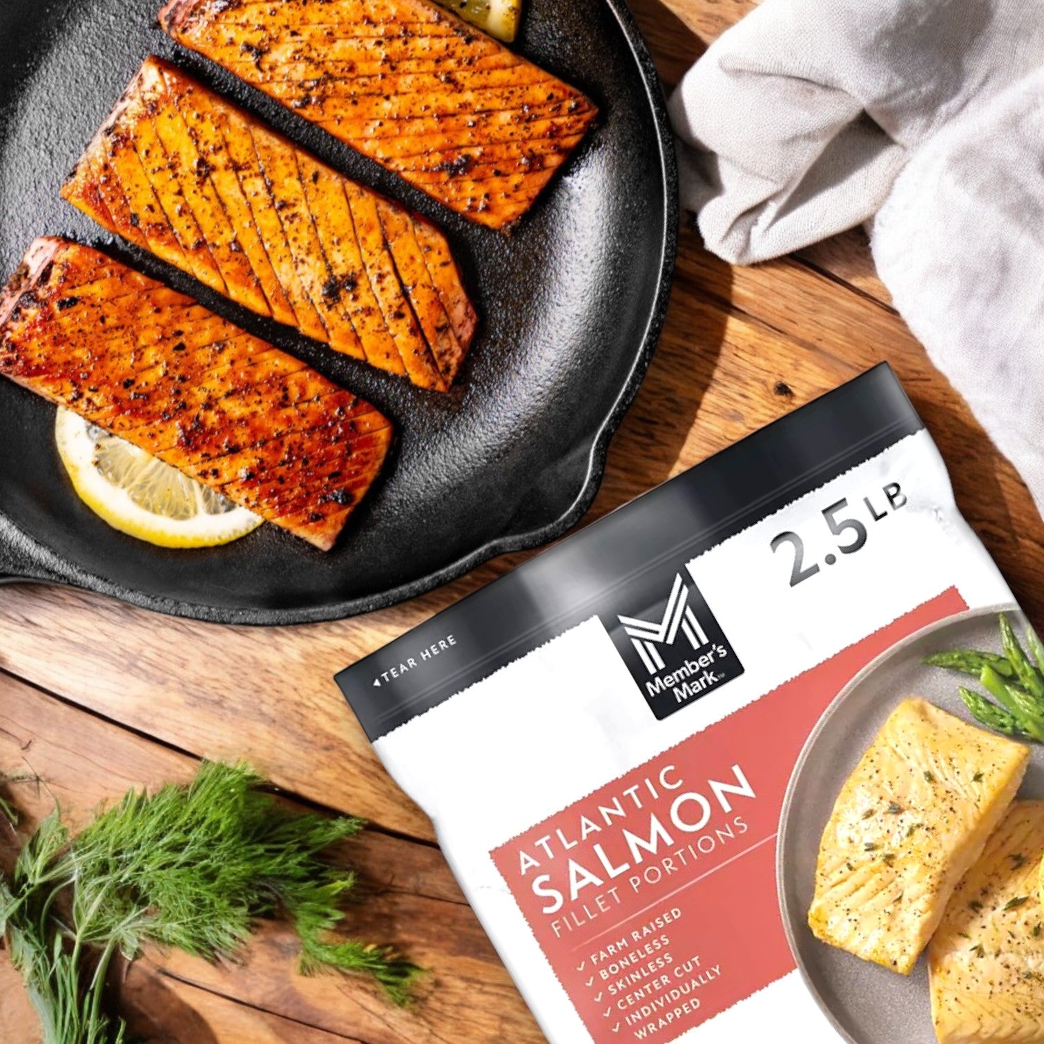 Four cooked Member's Mark Salmon Filet Portions on a skillet with lemon slices, the 40 oz. bag nearby, highlighting Omega-3 Fatty Acids benefits, set on a wooden surface with dill and a napkin.