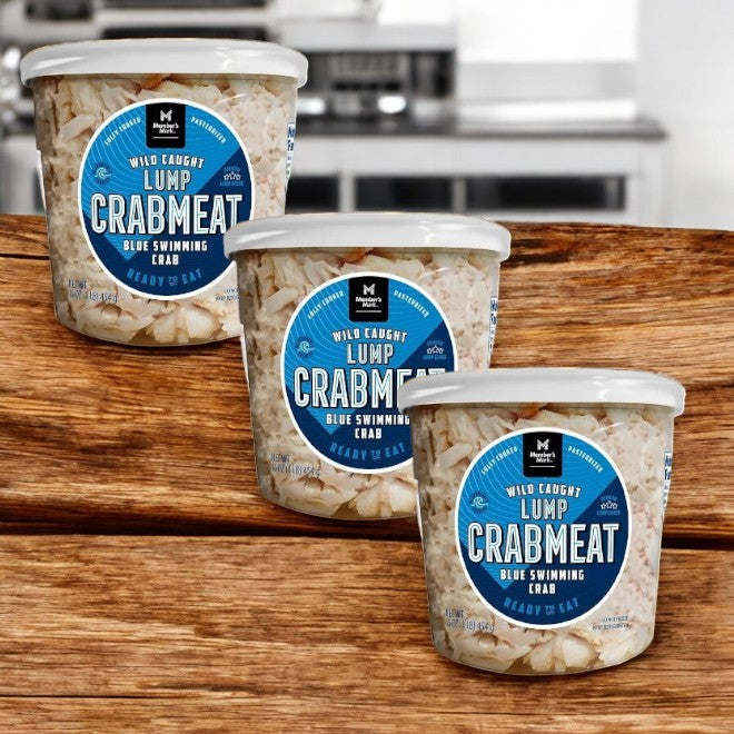 Three containers of Member's Mark Wild Caught Premium Lump Crab Meat, labeled as blue swimming crab and ready to eat, are placed on a wooden surface.