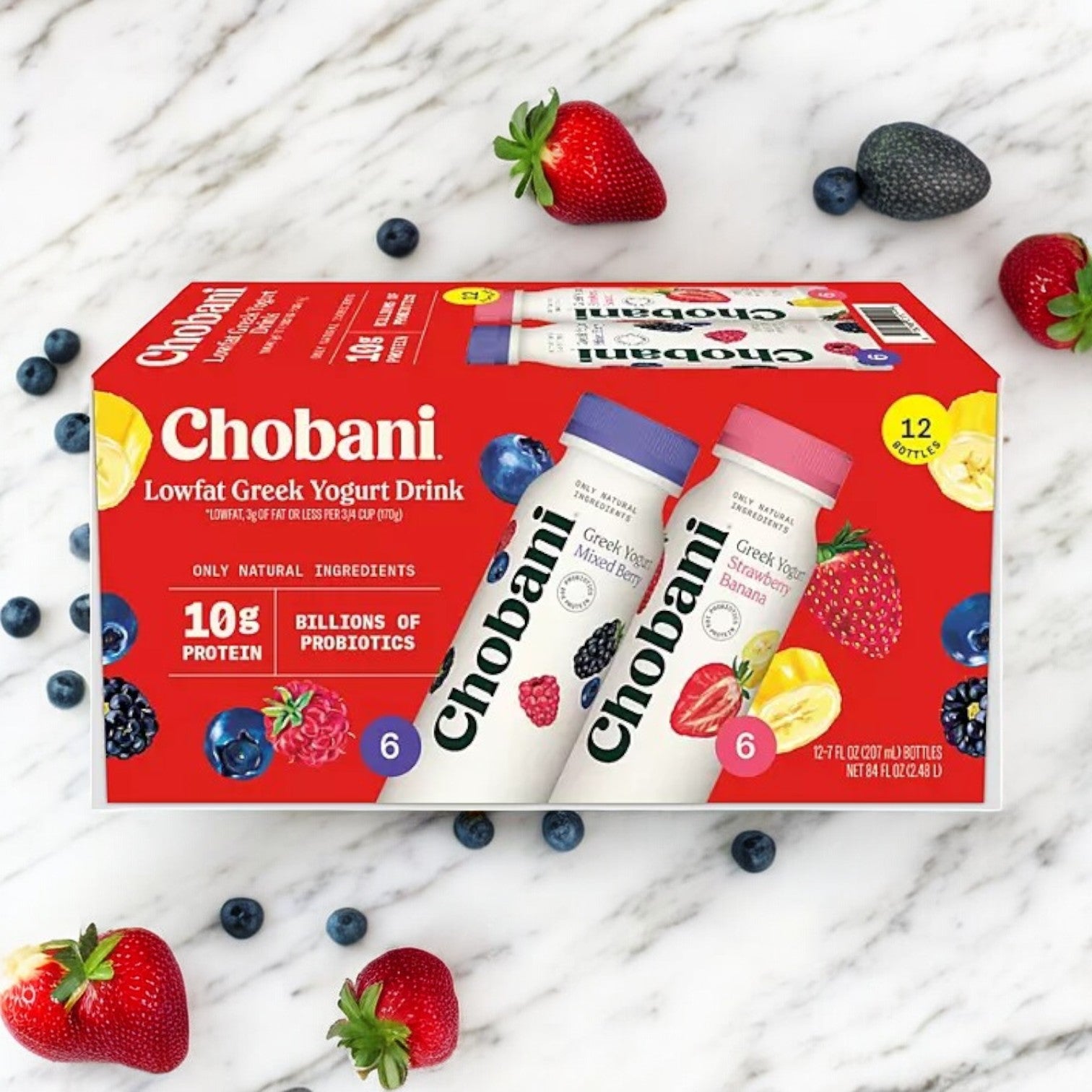 Chobani Lowfat Greek Yogurt Drink Variety Pack, 12 Ct- 1 Pack is displayed on a table amidst strawberries, blueberries, and bananas. The packaging highlights 10g of protein and billions of probiotics for a healthy boost.