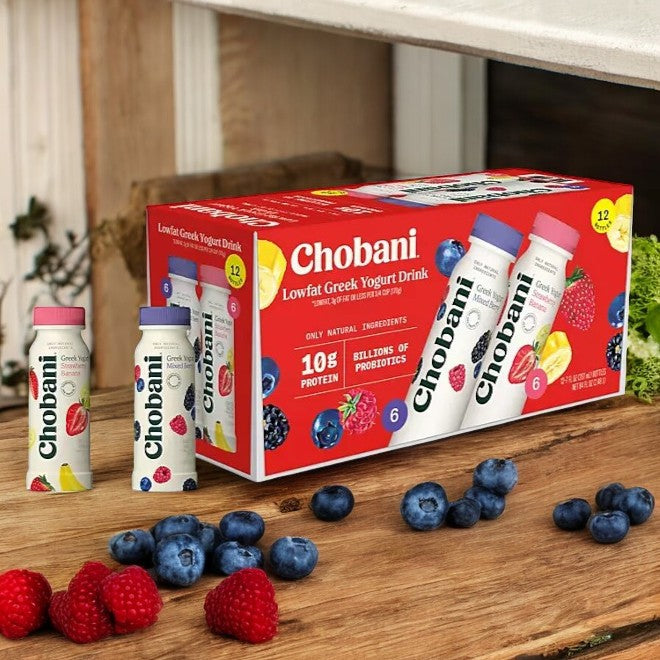 The Chobani Lowfat Greek Yogurt Drink Variety Pack, 12 Ct- 3 Packs, is attractively arranged with bottles upfront amid a vibrant display of fresh blueberries and raspberries on a rustic wooden surface, offering a delightful blend of protein and probiotics.
