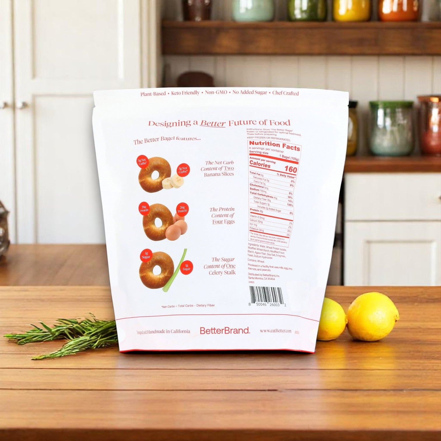 A white bag of BetterBrand’s The Better Bagel – Pretzel Style (4 bags, 16 bagels total) is displayed on a kitchen counter near rosemary and lemons, with its nutrition facts and healthy features shown on the back. In stock, ready to ship!.