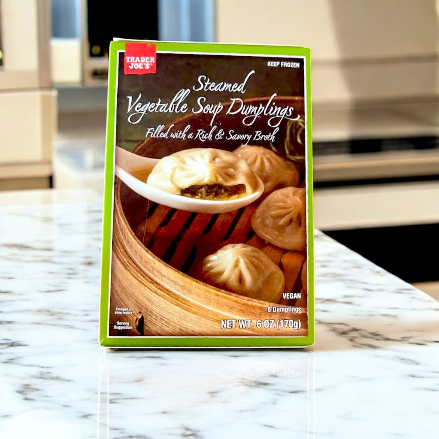 A box of Easy Lunches Steamed Vegetable Soup Dumplings – 6 oz. rests on the kitchen counter, highlighting an Asian cuisine favorite. The packaging displays dumplings in a bamboo steamer with the phrase "Filled with a rich & savory broth.