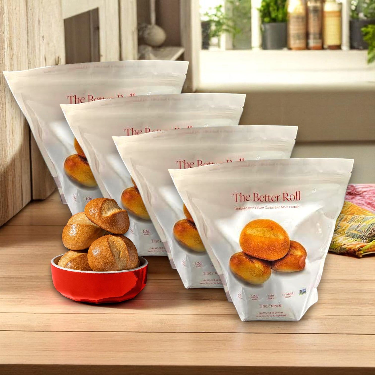 Four bags of BetterBrand’s The Better Roll – French Style (32 rolls total) are shown on a kitchen counter, with a red bowl of bakery-fresh French rolls in front. In stock and ready to ship!.