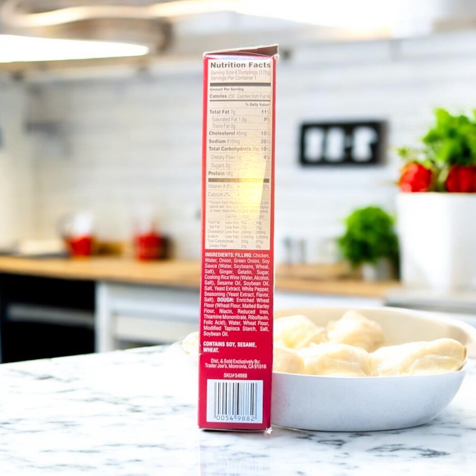 A box of Steamed Chicken Soup Dumplings by Easy Lunches sits on the kitchen counter, displaying its nutritional info. Beside it, a bowl with vibrant ingredients showcases crisp Green Pepper Julienne against a softly blurred kitchen background.