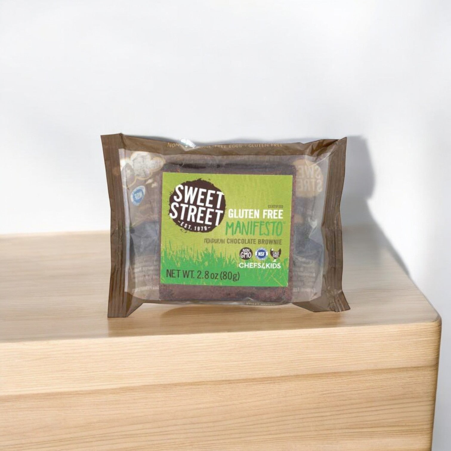 A Sweet Street Honduran Chocolate Manifesto Brownie, 3 oz., from a 48 per case pack, is displayed on a light wooden surface with a plain white background.