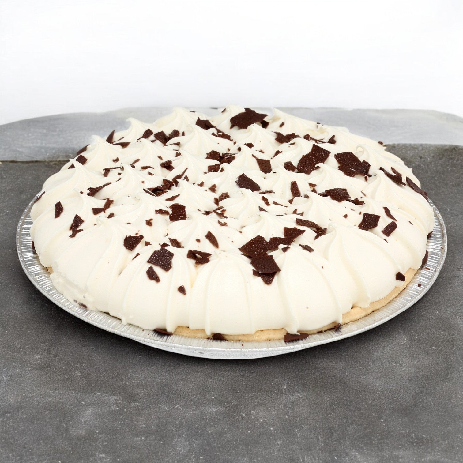 This decadent Sysco Imperial Assorted Cream Pie features a rich filling topped with delicate chocolate shavings, elegantly presented in a silver tin on a gray surface.
