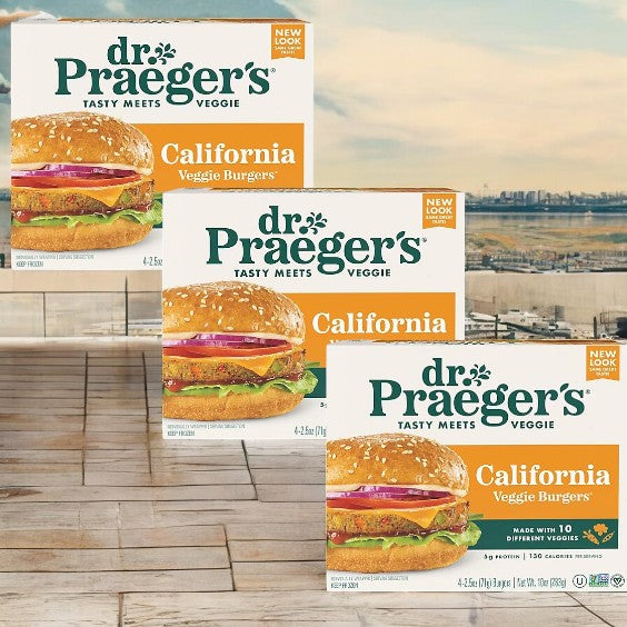 Three boxes of Dr. Praegers Burgers Veggie California Burger- 3 Count, a tasty meatless option, are showcased on a wooden surface with an urban skyline behind them.