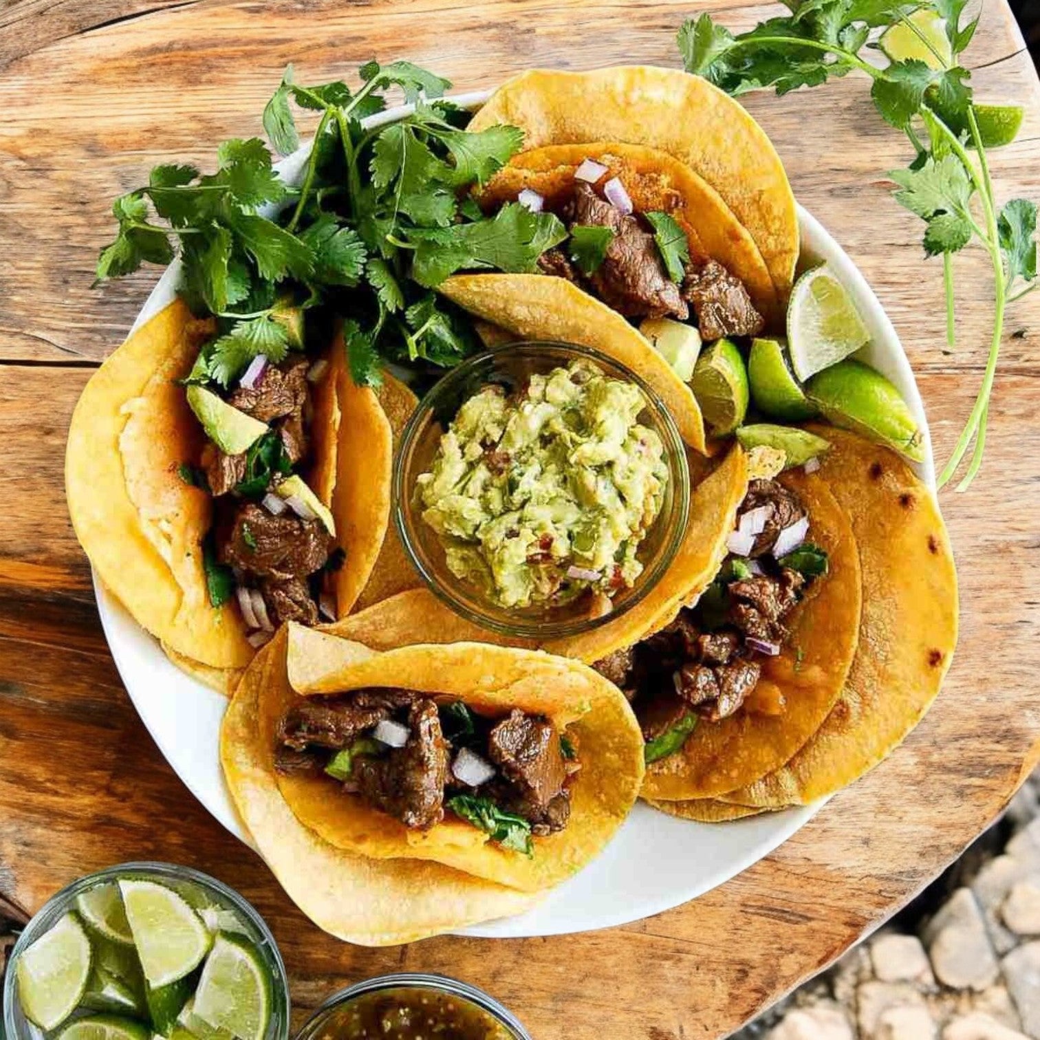 A plate of beef tacos made with El Milagro Yellow Corn Tortillas is served next to a bowl of guacamole, with lime wedges and fresh cilantro garnishing the wooden table.