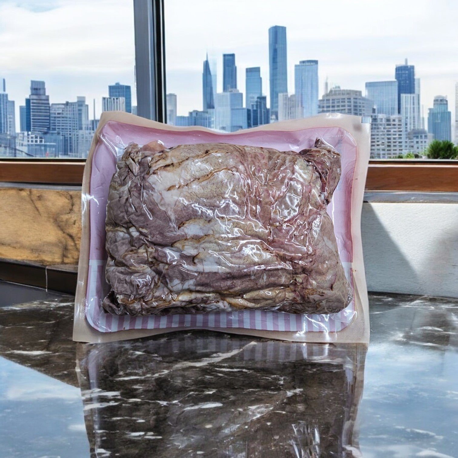 A Portillo's vacuum-sealed Italian Beef Gravy and 2 lbs. Take & Make Italian Beef package sits on a reflective surface with a city skyline visible through the window in the background, perfect for crafting Italian beef sandwiches.