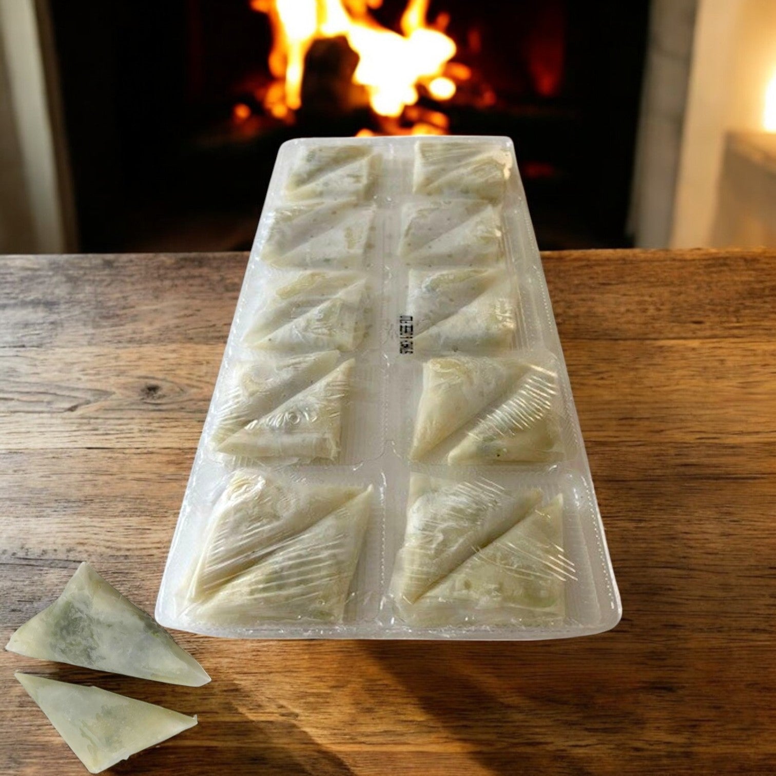 A tray from Portico Classic Seafood’s Sysco Imperial Spanakopita Appetizer—one of five frozen trays with 20 flaky phyllo-wrapped pieces—is displayed on a wooden table by the fireplace, with two spanakopita placed outside the tray.