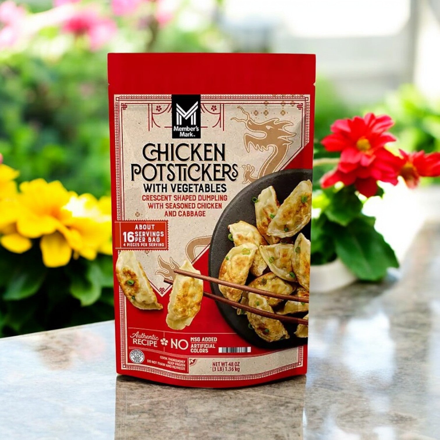 A 48 oz case of Member's Mark Chicken Potstickers with Vegetables sits outdoors on a stone surface, surrounded by flowers and greenery.