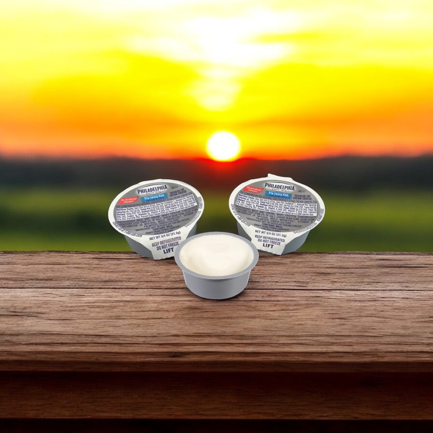 Three 4 oz containers of Kraft's Philadelphia Cheese Cream Light rest on a wooden surface, illuminated by the golden glow of a sunset, ideal for portion control in every bite.