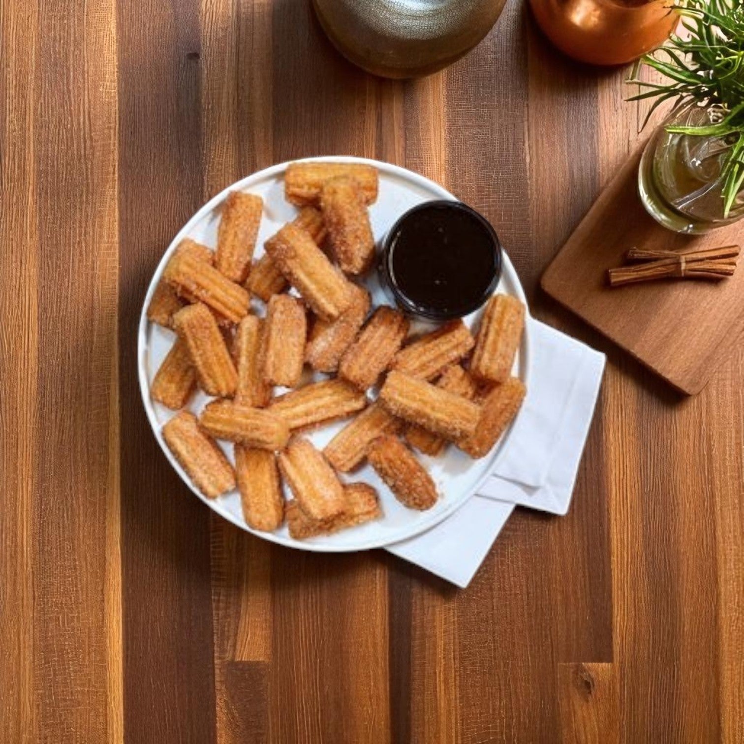 A white plate of Hola Churro® – Mexican Mini Churros (2") by Hola Churro sits on a wooden table, dusted in sugar and served with chocolate sauce, with a napkin underneath.