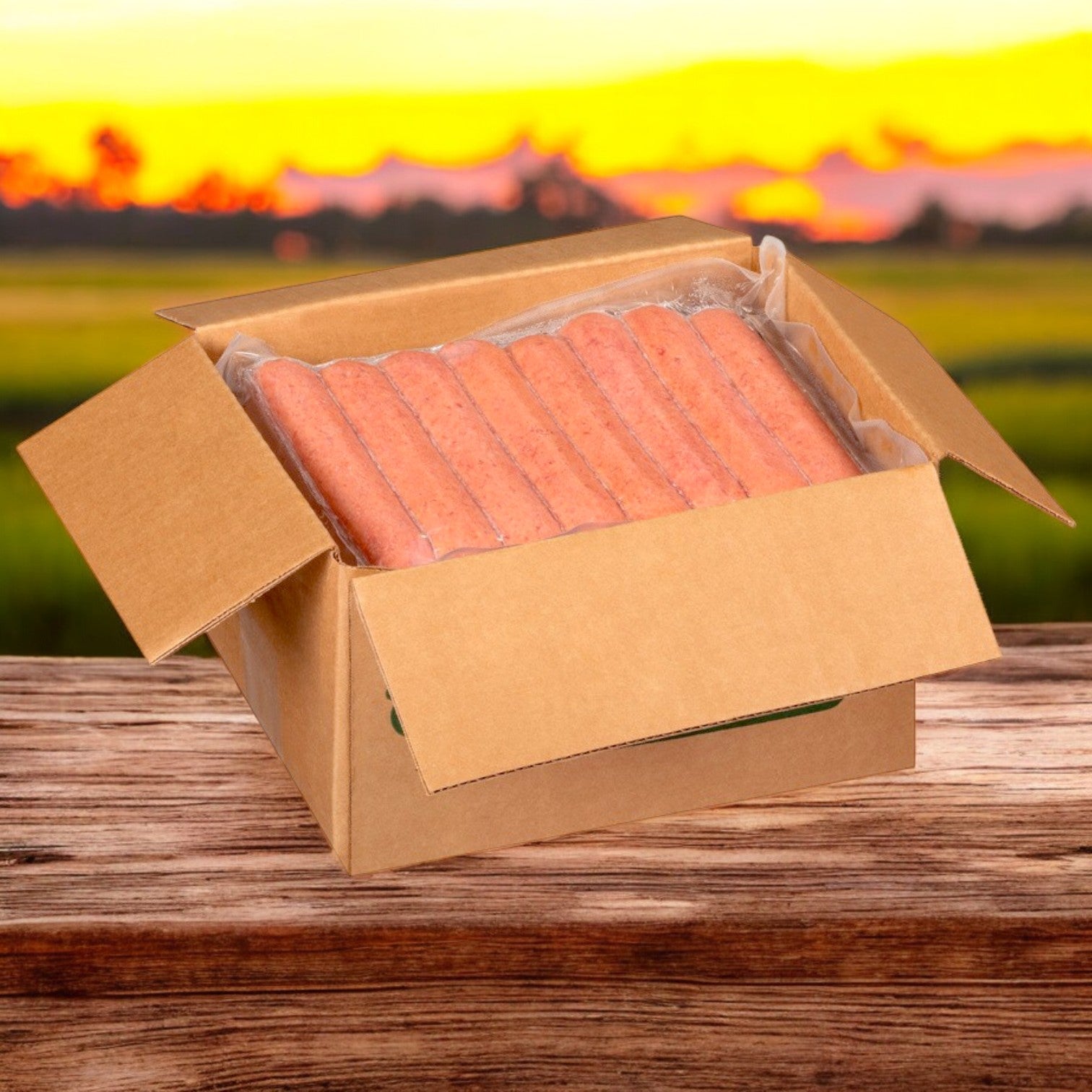 An open cardboard box of Nathan’s Famous Sausage Polish – 10 LB- 50 Franks In Each Case rests on wood, framed by a vibrant sunset and fields, highlighting their premium quality amid nature's splendor.