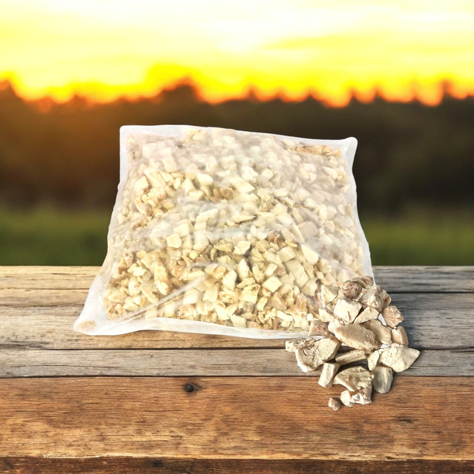 A sealed clear plastic bag filled with Sysco's diced chicken meat, featuring low sodium white and dark pieces, rests on a wooden table. Some pieces lie outside the bag against a serene blurred sunset landscape backdrop.