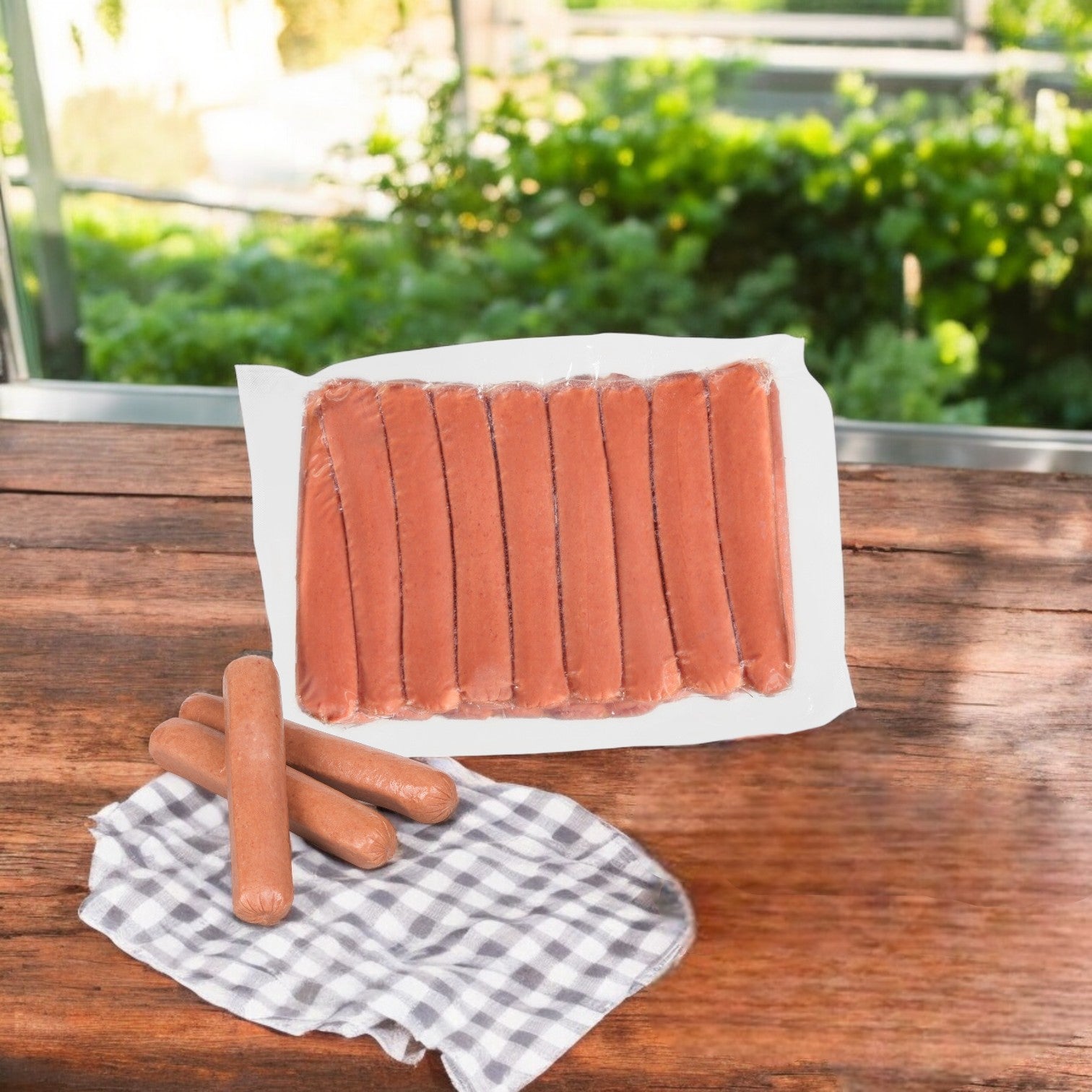 A 10-lb package of Nathan's Famous All-Beef Frankfurters (50 hot dogs, 2 bags) sits on a wooden table, with three 6-inch hot dogs and a checkered cloth nearby. Greenery can be seen in the background.