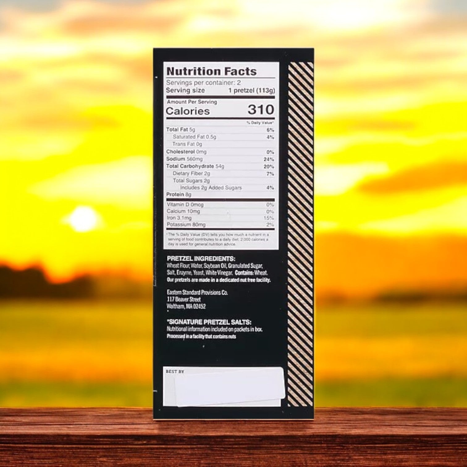 A box showing the nutrition facts and ingredients for Easy Lunches Eastern Standard Provisions Signature Soft Artisanal Handcrafted Pretzels, 2 ea - 3 Packs, set before a blurred sunset background.