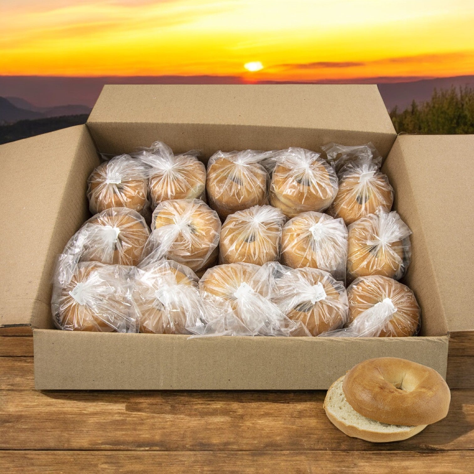 A cardboard box of Lender's Bagel Classic Brat & Sausage Hinged Buns (8 packs, 64 total) sits on a wooden surface, next to a sliced bun and a sunset in the background.
