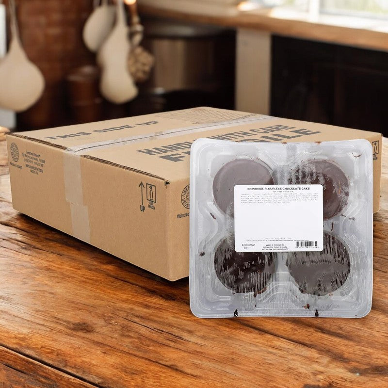 Eight clear plastic packs of Sweet Street Cake Chocolate Flourless (gluten-free), each containing 4 cakes, are arranged in front of a large cardboard shipping box on a wooden kitchen counter. Total: 32 cakes per case.