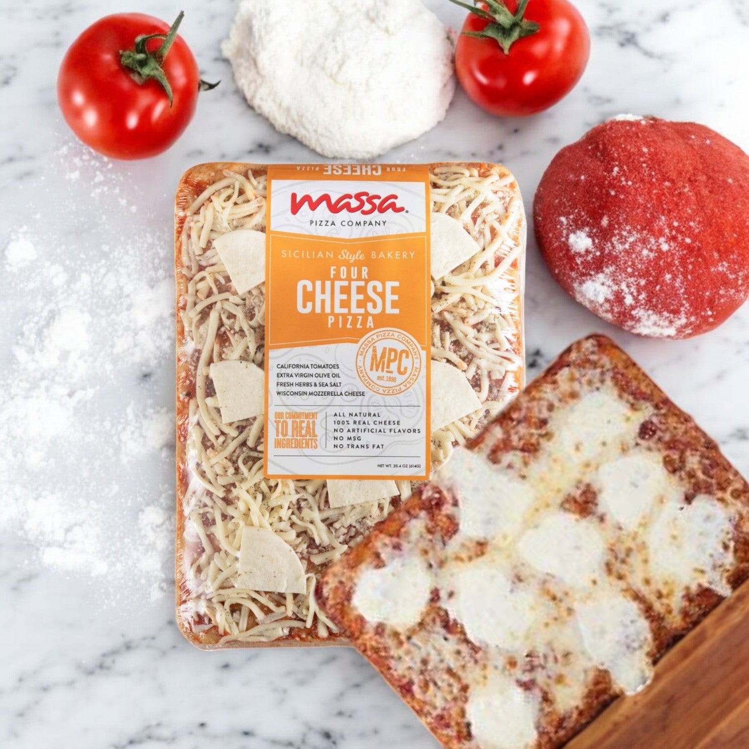 A box of Massa Pizza Co. Four Cheese Sicilian Bakery Pizza, 23.1 oz., is displayed on a marble surface with tomatoes, dough, flour, and a slice of baked pizza around it.