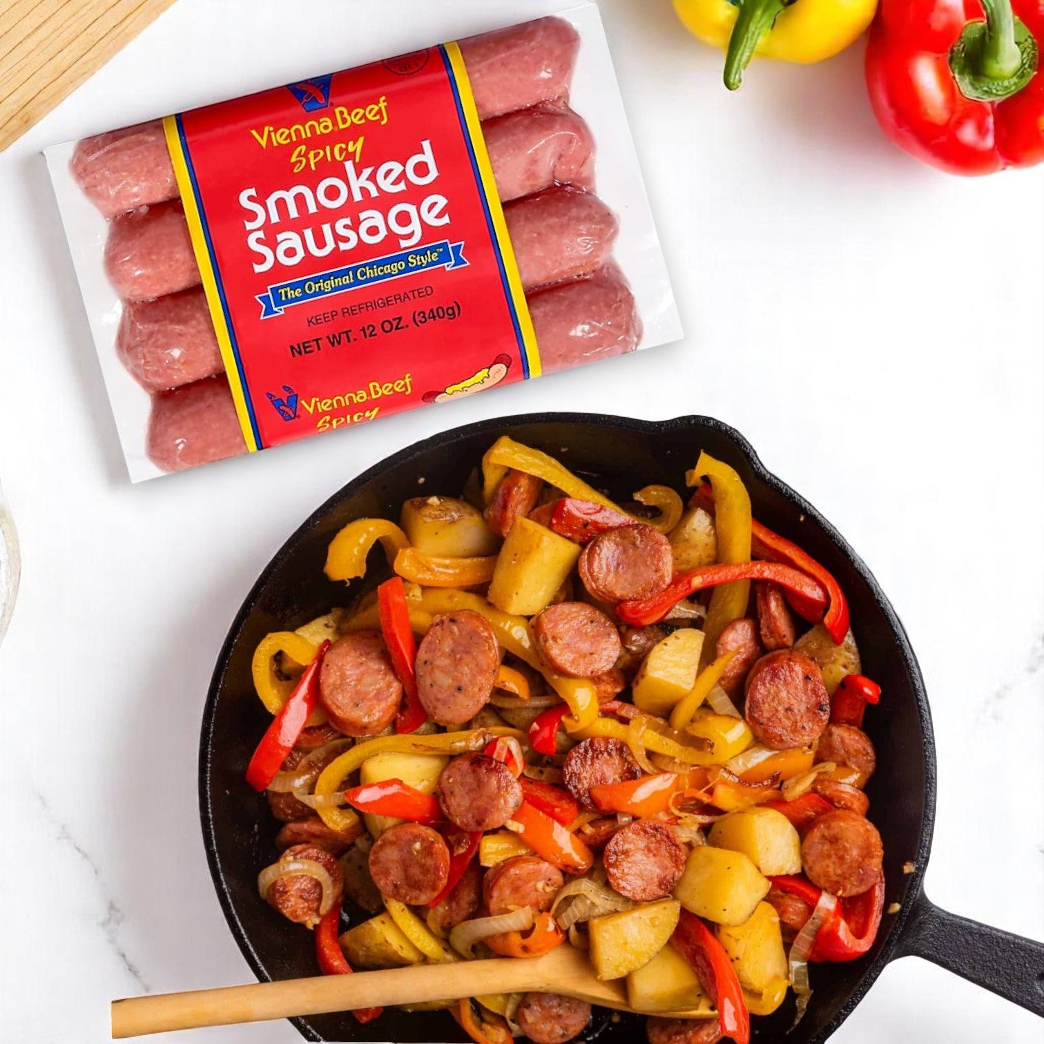 A skillet with sliced Vienna Beef Spicy Skinless Smoked Sausage, potatoes, and bell peppers sits below a package of Vienna Spicy Skinless Smoked Sausage – 3-Pack, 12 oz each, on a white surface.