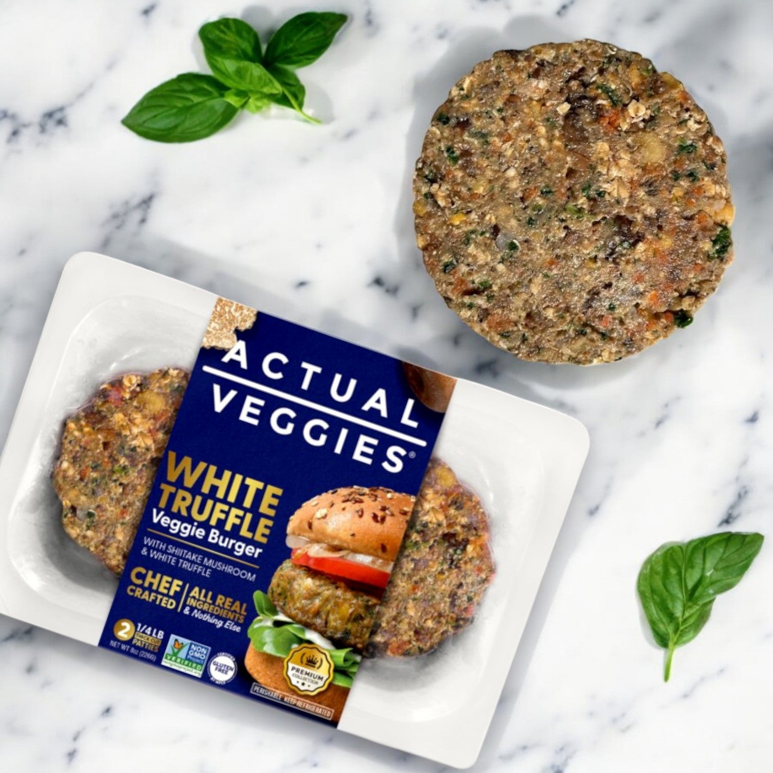 Actual Veggies White Truffle Veggie Burger patties are displayed on white marble; one labeled patty highlights its gluten-free benefits, while another is placed nearby. Fresh basil leaves add a decorative touch.