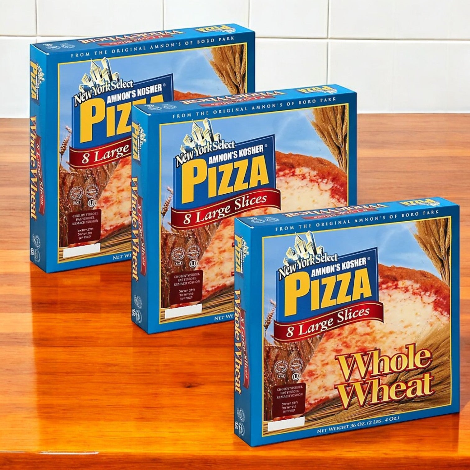 Three boxes of Amnon's Kosher Pizza Whole Wheat Frozen 36 oz., each with large slices, are displayed on a wooden surface.