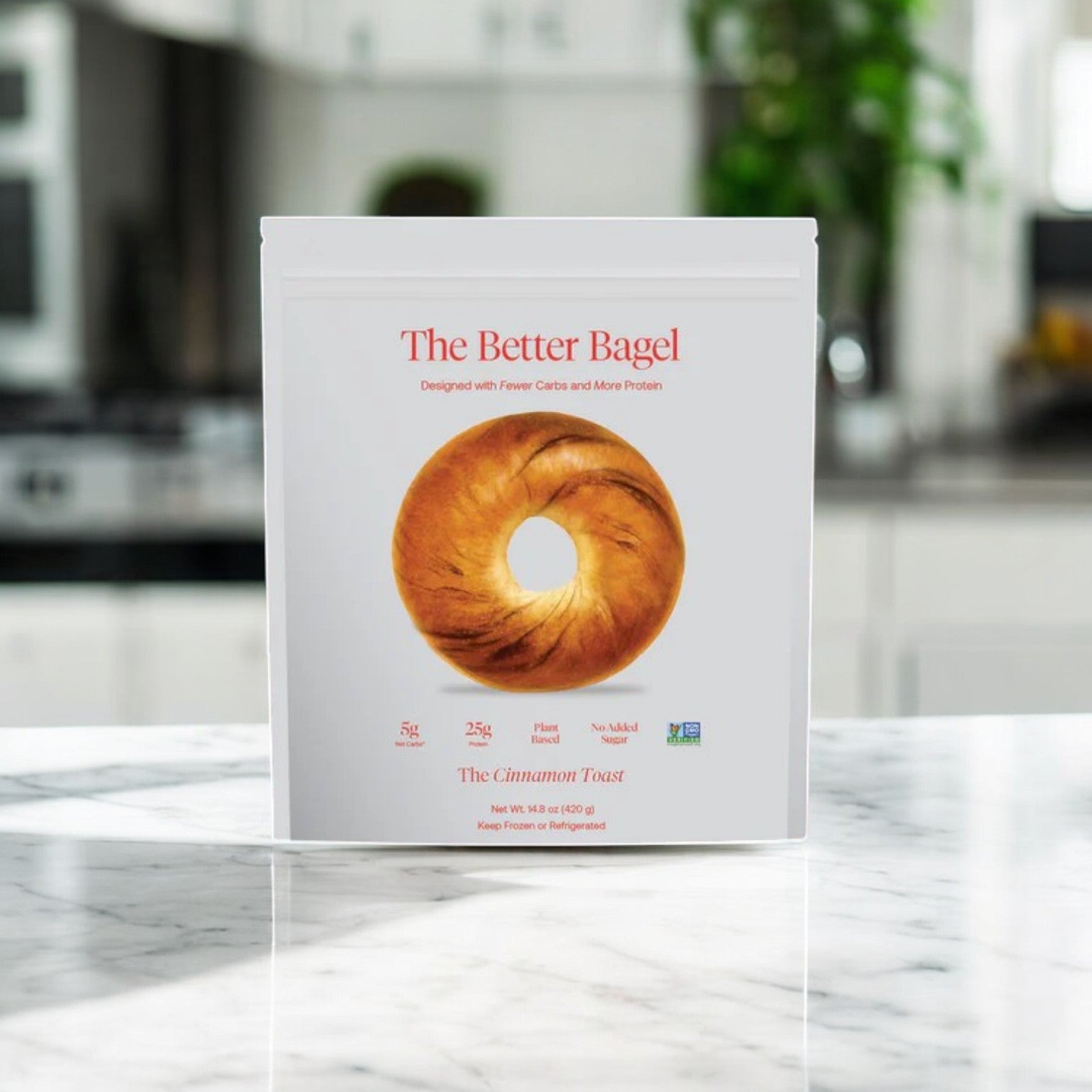 A white bag labeled "Better Brand – The Cinnamon Better Bagel" (1 bag, 4 total bagels) with Low-Carb and High-Protein highlights is shown on a kitchen counter, background blurred. In stock and ready to ship from BetterBrand!.