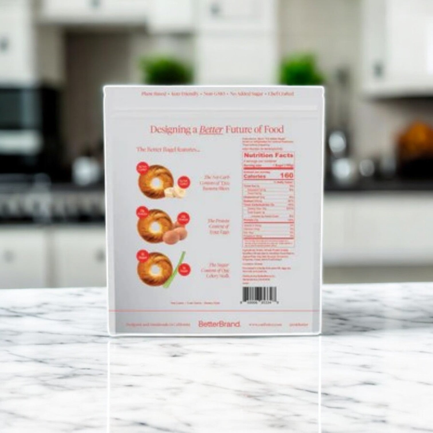 A box of BetterBrand – The Cinnamon Better Bagel (1 bag, 4 total bagels) sits on a marble kitchen countertop, displaying the back panel with product info and nutrition facts. In stock and ready to ship!.