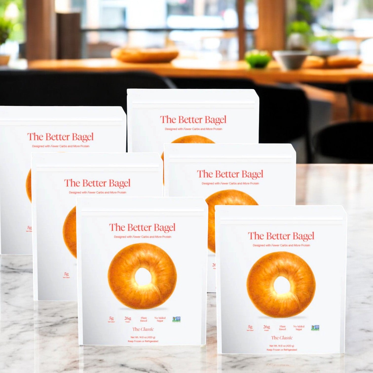 Six bags of BetterBrand’s The Classic Better Bagel (24 bagels total) are displayed on a marble countertop in a bright kitchen, highlighting their high protein classic flavor, with fresh bagels and plants in the background. In stock and ready to ship!.