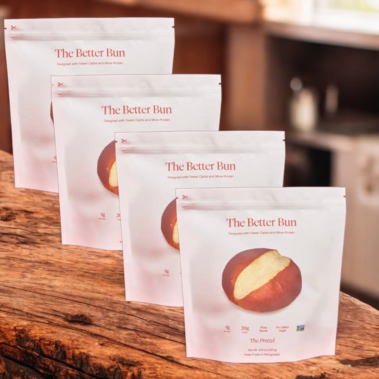 Four packages of BetterBrand’s The Better Bun – Pretzel Style (4 bag, 16 bagels) are arranged in a row on a wooden surface, each featuring the product’s pretzel-style bagel packaging. In stock and ready to ship!.