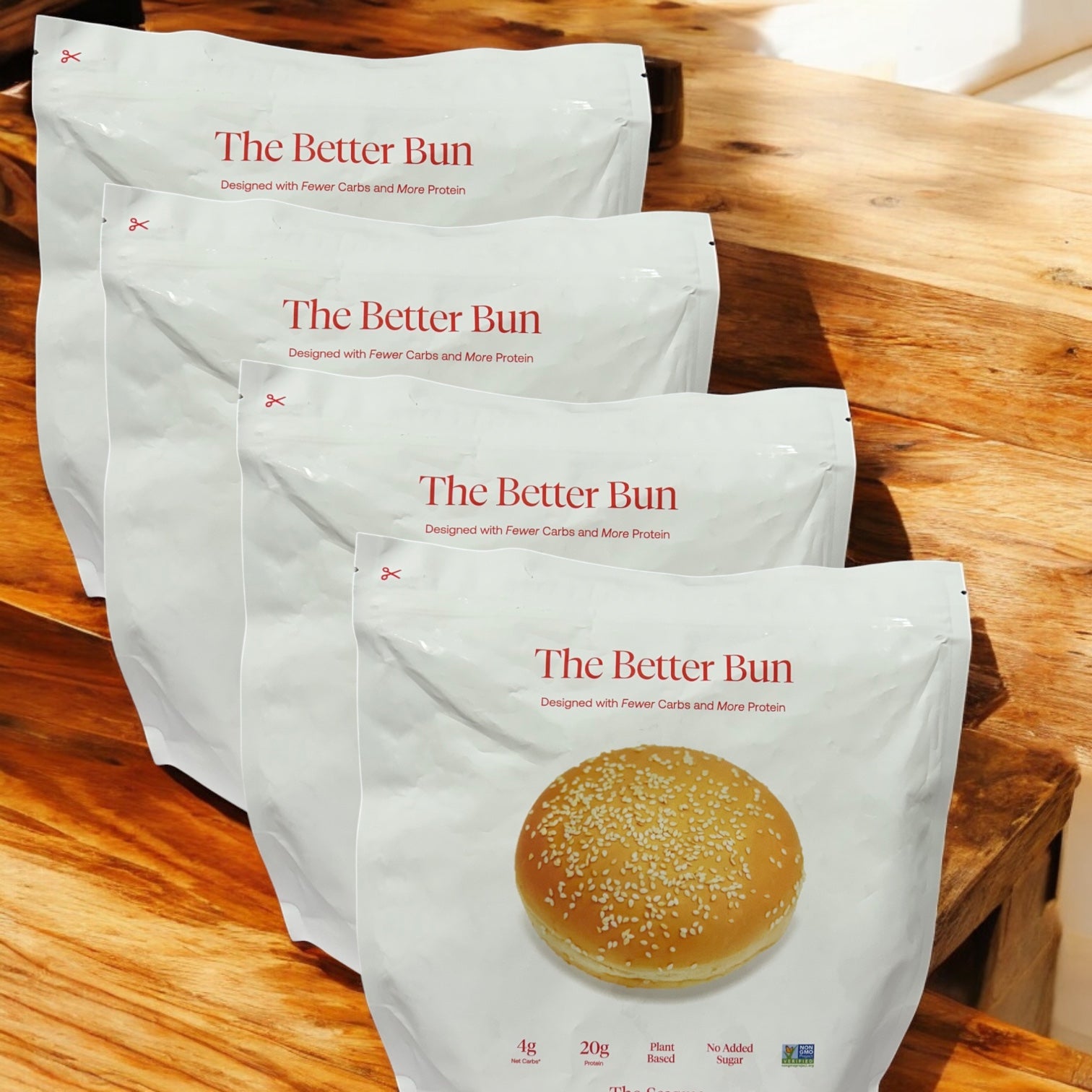 Four packages of BetterBrand’s The Better Bun – Sesame Style (16 bagels total) are arranged on wood—ideal for anyone seeking high protein and low net carbs in every bite. In stock and ready to ship!.