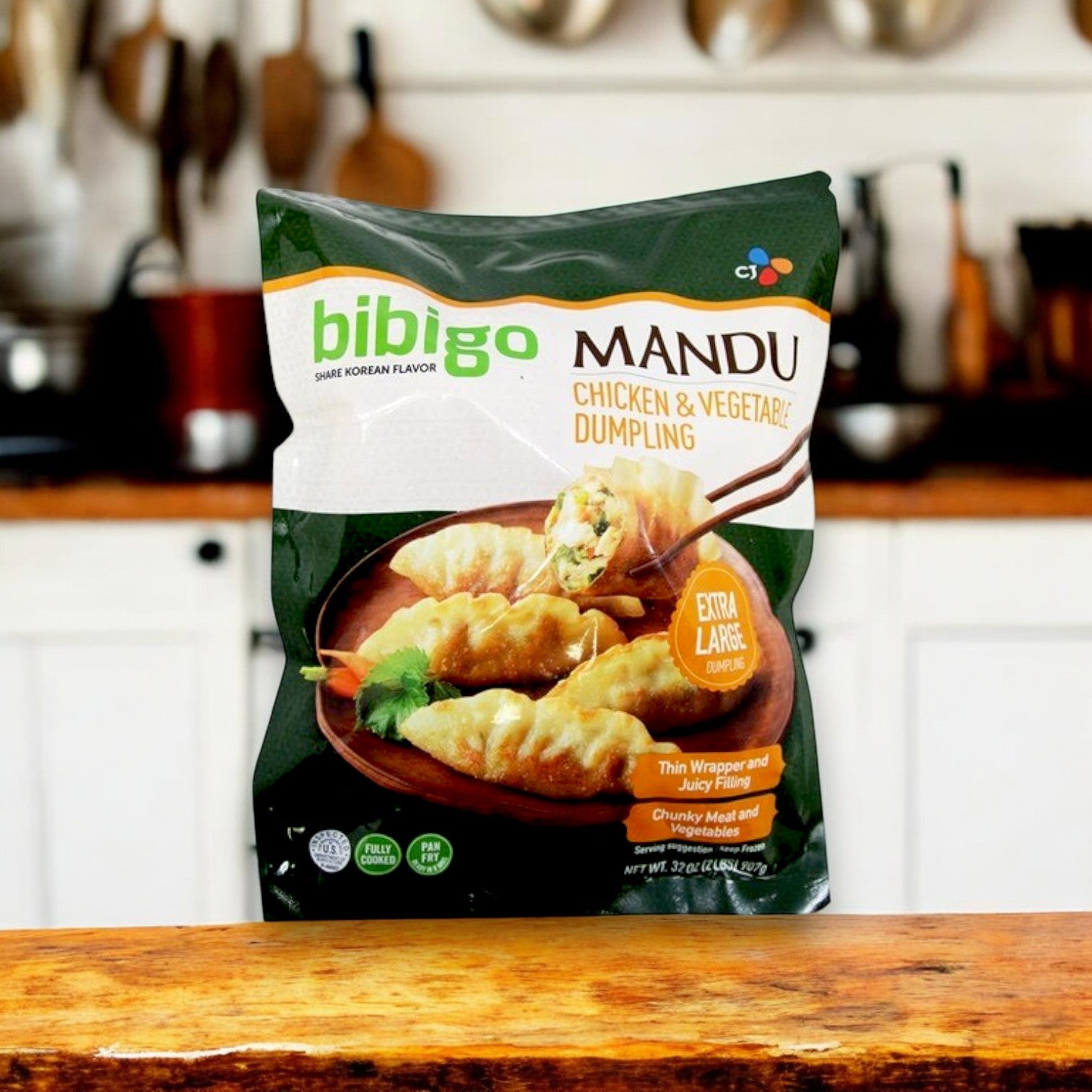 A bag of Bibigo Chicken & Vegetable Mandu Dumpling | 32 oz. - 3 Packs rests on a wooden counter in a kitchen, with the background softly blurred.