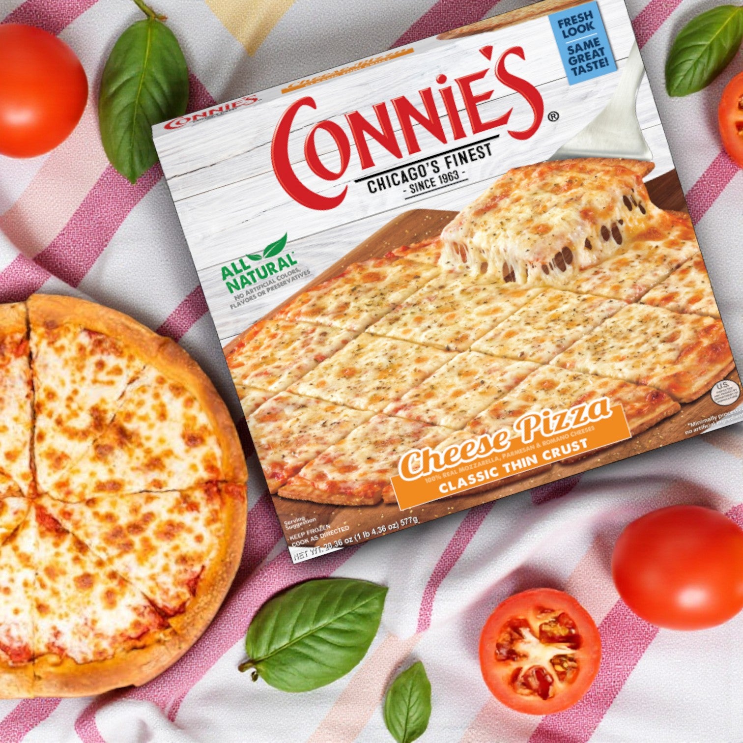 A Connie's Pizza Classic Thin Crust Combo – 3 Pack! box sits on a cloth beside a classic thin crust pizza, fresh tomatoes, and basil leaves.