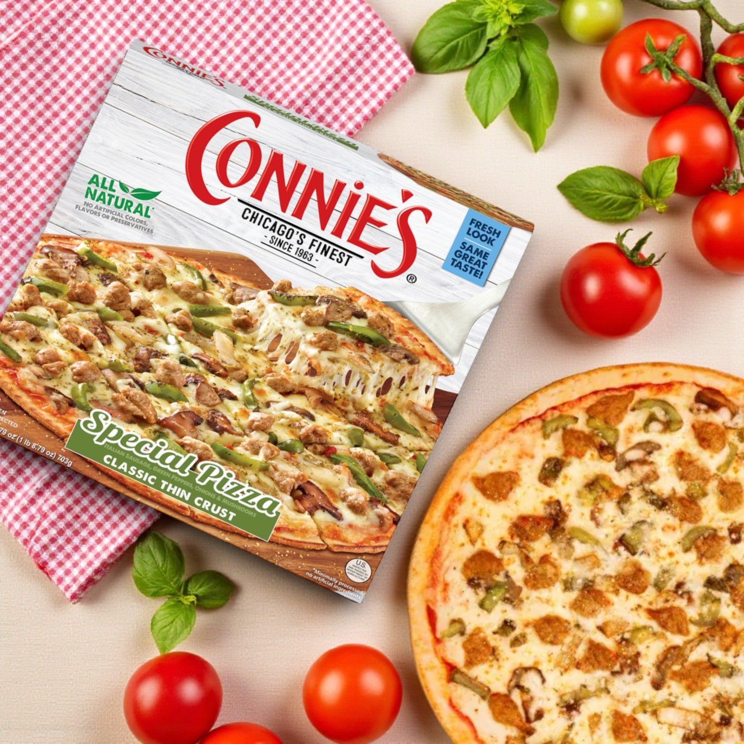 A Connie's Pizza Classic Thin Crust Combo – 3 Pack! sits beside a baked classic thin crust pizza, surrounded by fresh tomatoes and basil on a wooden surface.