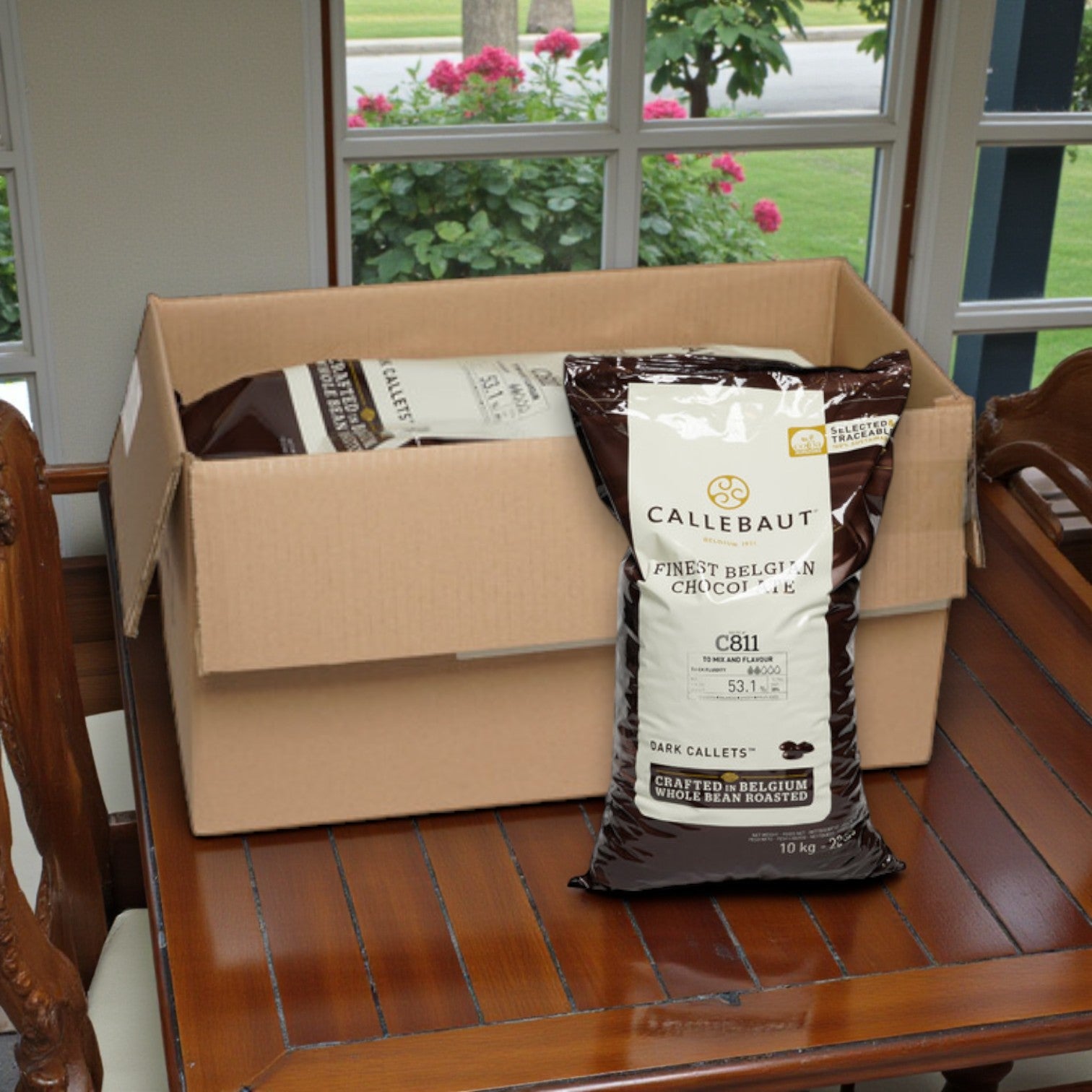 A box of Callebaut Chocolate Dark Callets 53.1% – 1/10 KG is placed on a wooden dining table near a window.