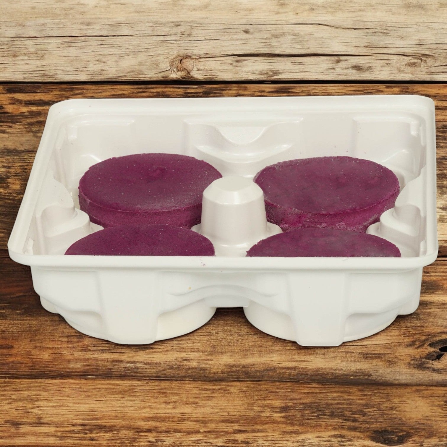 A white plastic tray with four Sweet Street Ube Cheesecakes (4.03 oz each) sits on a wooden surface, highlighting their authentic ube flavor. Sold as 1 case (32 cheesecakes). Allow 2–3 extra business days for processing before shipping.