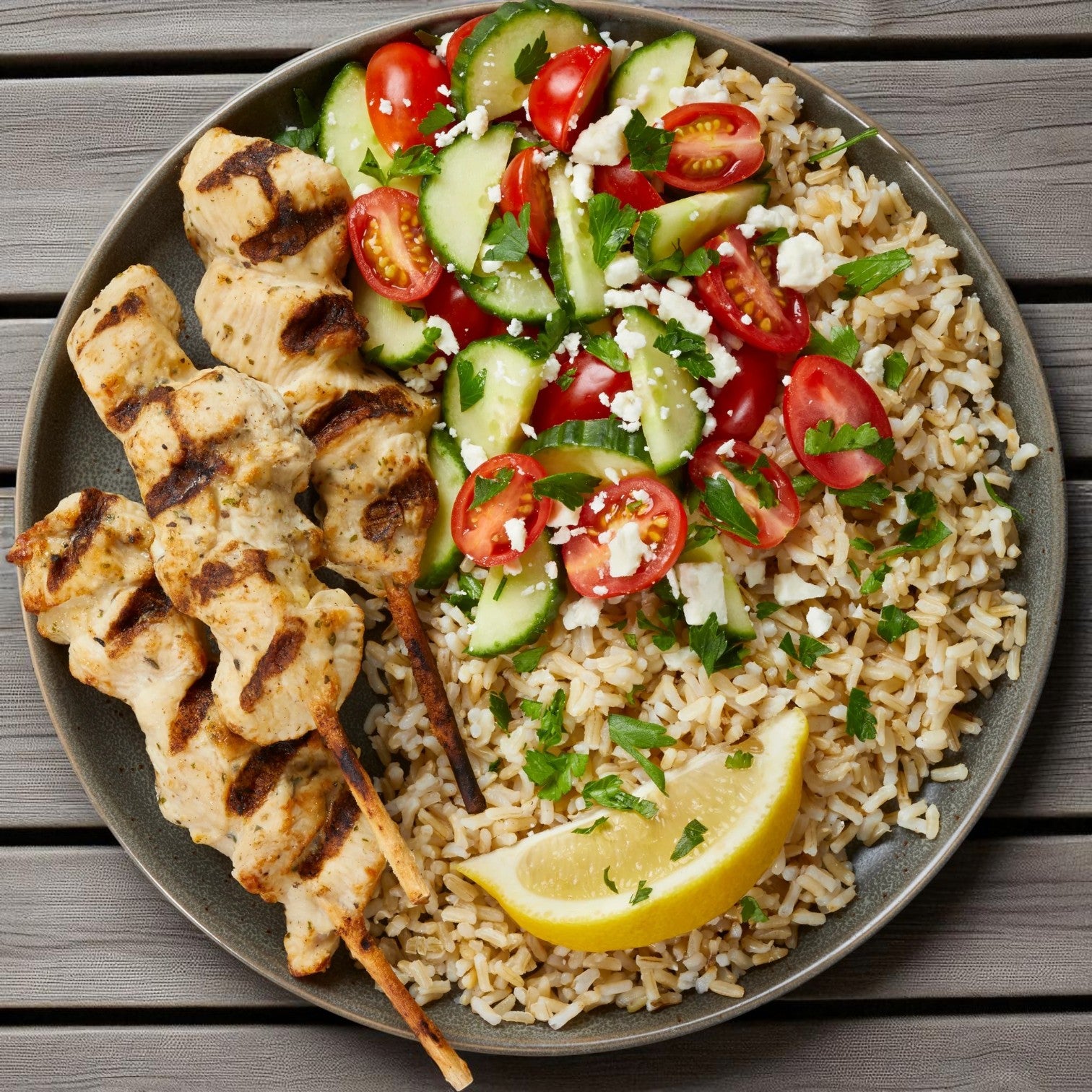 Enjoy Gordon Choice: two skewers of juicy grilled chicken breast with brown rice, cucumber-tomato salad topped with feta, and lemon wedges. Perfect as a high-protein snack or meal from the Gordon Choice brand.