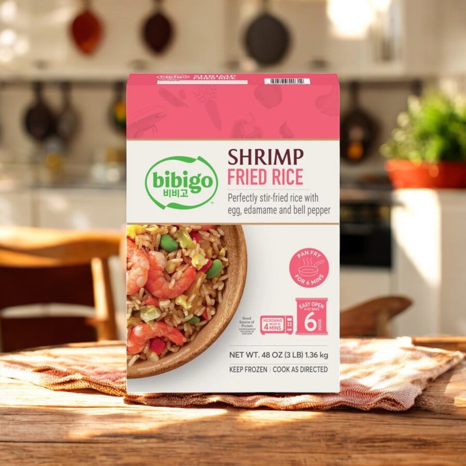 A box of CJ Bibigo Shrimp Fried Rice, 8 oz, 6-Count by Bibigo rests on a wooden table in a sunlit kitchen.