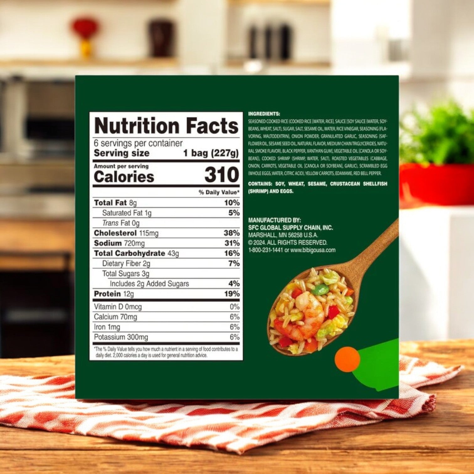 A close-up of a CJ Bibigo Shrimp Fried Rice, 8 oz, 6-Count package by Bibigo, with Korean seasoning, nutrition facts, ingredients, and a small image of the cooked dish on a wooden counter and a blurred kitchen background.