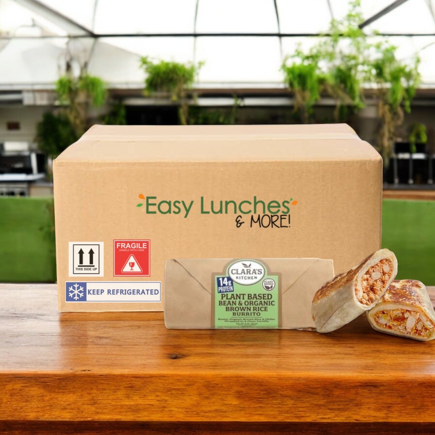 A cardboard box with "Easy Lunches & More!" contains a Clara's Kitchen Individually Packaged Vegan Bean & Cheese Burrito, 8 oz., showcasing its plant-based cheese and organic brown rice filling. The burrito is partially sliced to reveal the hearty contents.