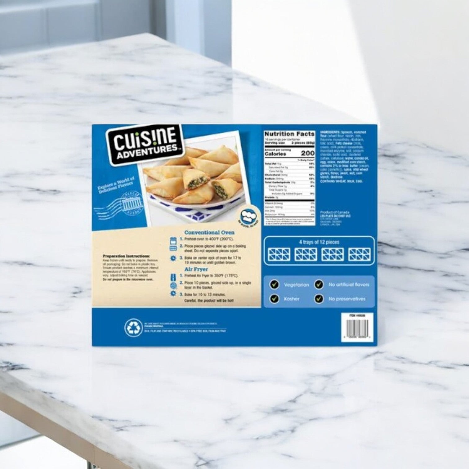 On a marble surface, the back of the Cuisine Adventure's Spanakopita Spinach & Feta Phyllo Triangles package displays product details, nutrition facts, cooking instructions, and dietary icons. Inspired by Mediterranean cuisine, its spinach and feta offer a delightful twist on tradition.