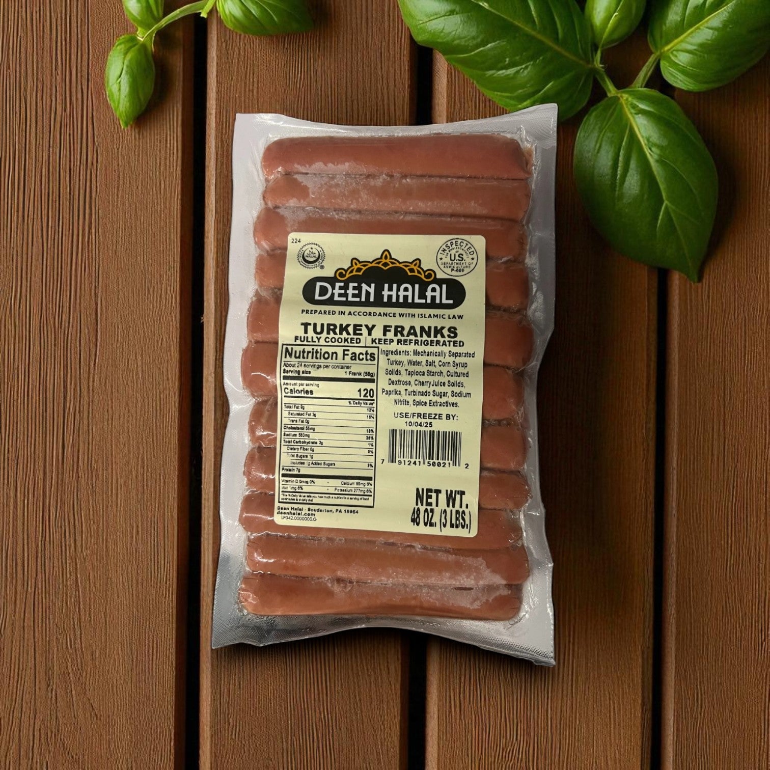 A sealed 48 oz (3 lbs), 24 count pack of Deen Halal Turkey Franks from Deen Halal is displayed on a wooden surface with fresh basil leaves nearby.